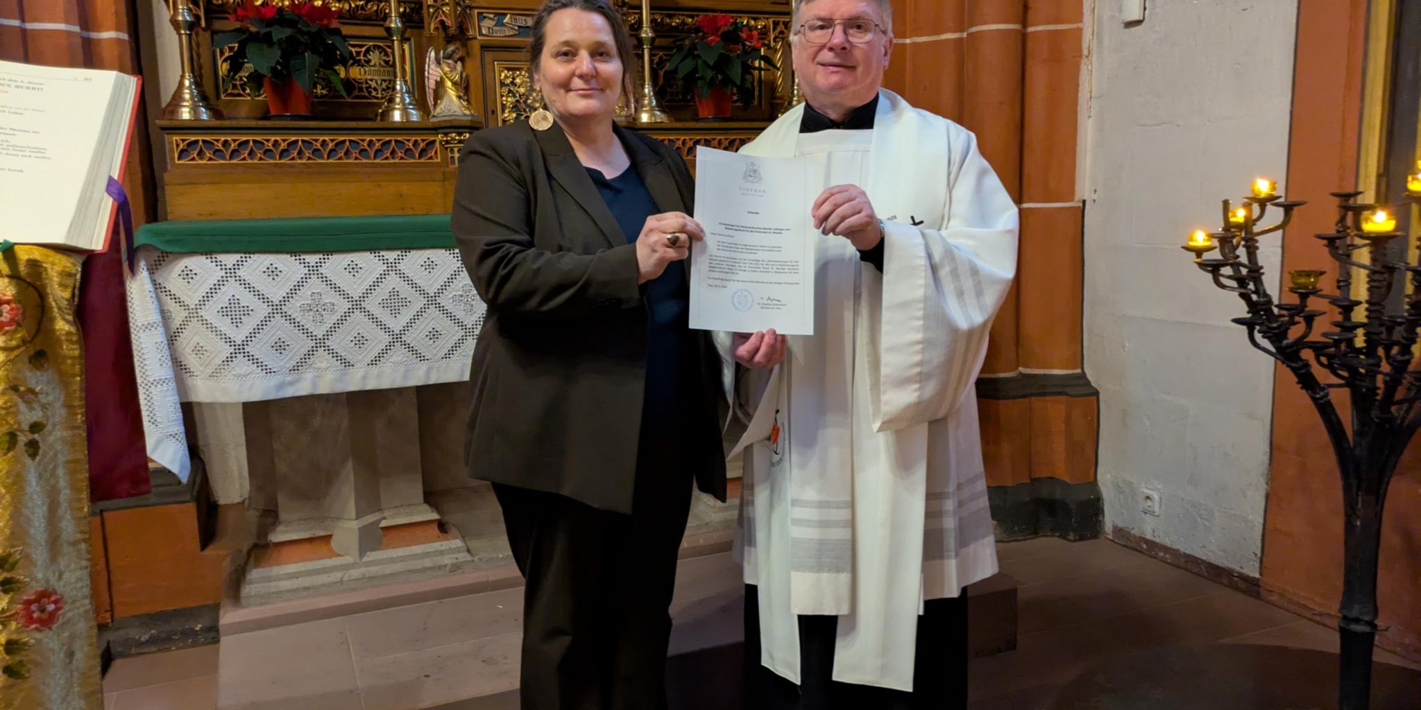 Vor dem Marienaltar der Basilika St. Wendel stehen Dekan Leist und Monika Leidinger mit einer Urkunde