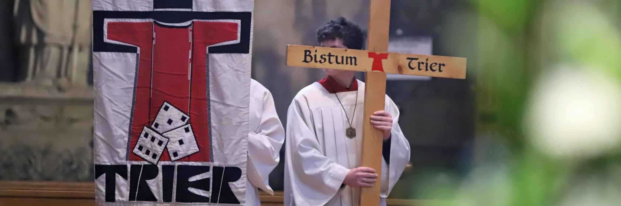 Zwei Messdiener in einer Messe; einer hält die Pilgerfahne mit der Aufschrift 'Trier' hoch, der andere ein Kreuz, auf dem Bistum Trier steht. (c) Bistum Trier/Inge Hülpes Zwei Messdiener in einer Messe; einer hält die Pilgerfahne mit der Aufschrift 'Trier' hoch, der andere ein Kreuz, auf dem Bistum Trier steht.